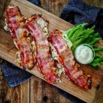 Tre fyllda baconskivor placerade på en träskärbräda med en skål sås och sallad.