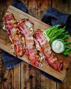 Tre fyllda baconskivor placerade på en träskärbräda med en skål sås och sallad.