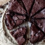 En kladdkaka skuren i åtta bitar på ett bakplåtspapper med en kniv bredvid.