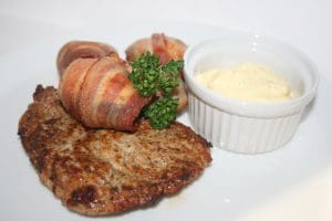 Grillad köttbit med baconlindade champinjoner och en skål med sås på en tallrik.