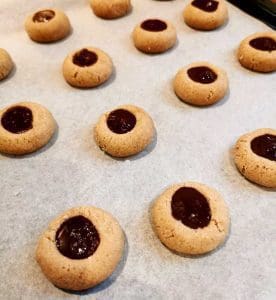 Runda kakor med en chokladfyllning i mitten, placerade på en bakplåt med bakpapper.
