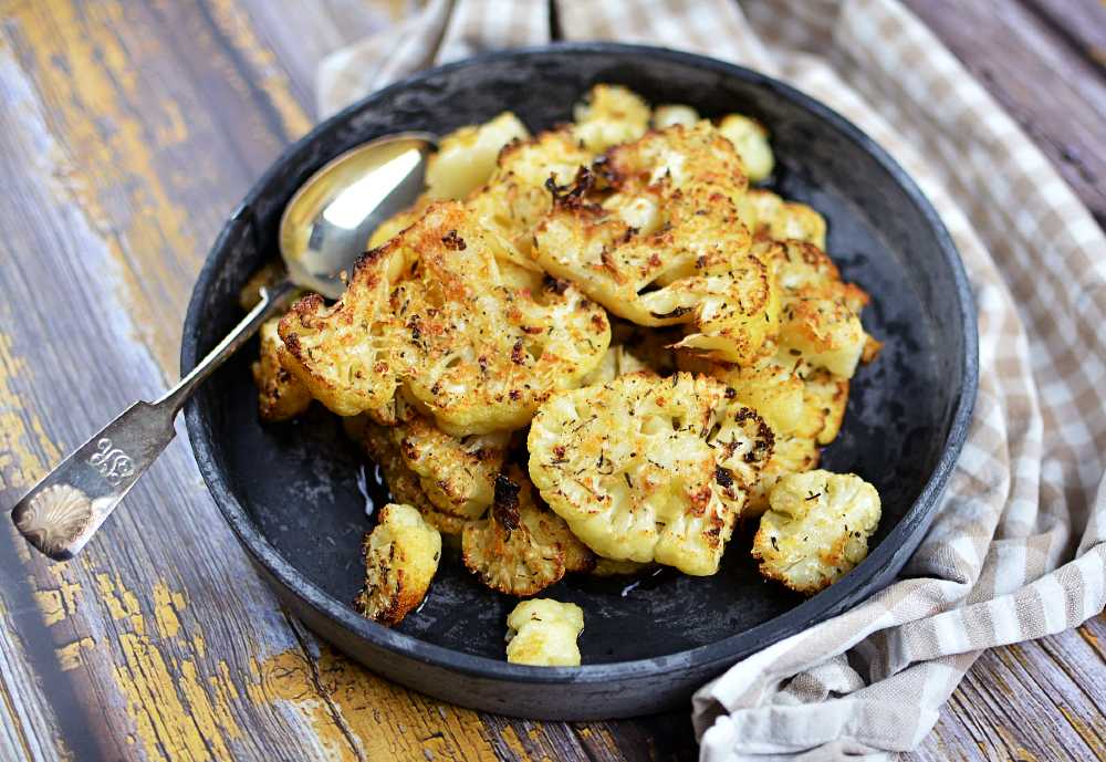 Ugnsrostad blomkål med parmesan och vitlök 6 En mörkgrå tallrik med ugnsrostad blomkål i på en gammal träbänk