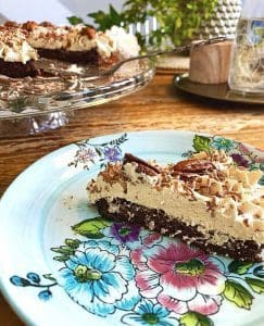 En skiva kladdkaka med fluffig topping och hackade nötter på en blommig tallrik.
