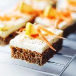 En bit morotskaka med vit glasyr och dekoration av morotsstrimlor och en bit frukt.