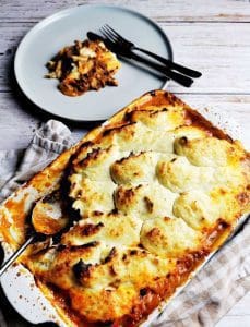 En ugnsform med Shepherd's Pie toppad med gyllenbrunt potatismos, serverad med en portion på tallrik.