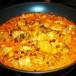 En stekpanna med köttbitar i en krämig sås med lingon och kryddor.