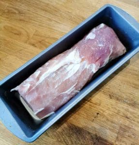 En köttbit placerad i en grå ugnsform på en träyta.