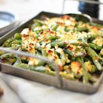 Ugnsbakad haricots verts med fetaost i en metallform på ett bord.