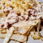 Tallrik med ost- och skinksås över grönsaker och pasta.