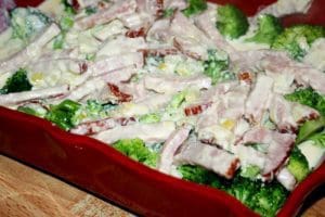 En maträtt med kassler och broccoli täckt av en krämig sås i en röd ugnsform.