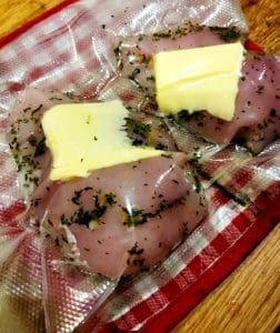 Vakuumförpackade kycklingfiléer med kryddor och smör på en röd och vit rutig duk.
