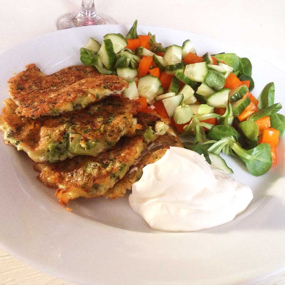 Blomkålsbiffar med parmesan 5 Tre broccolibiffar serverade med grönsallad och en klick gräddfil på en vit tallrik.