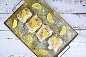 Flera bitar av ugnsbakad torsk med citronskivor på en plåt.