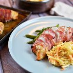 Baconlindad kycklingfilé serverad med grönsaker och coleslaw på en tallrik.