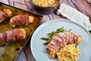 Baconlindad kycklingfilé serverad med grönsaker och coleslaw på en tallrik.