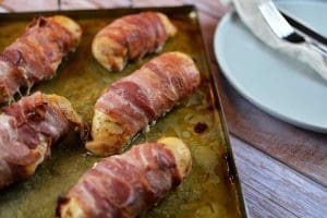 Baconlindade kycklingfiléer som ligger på en bakplåt med fett.