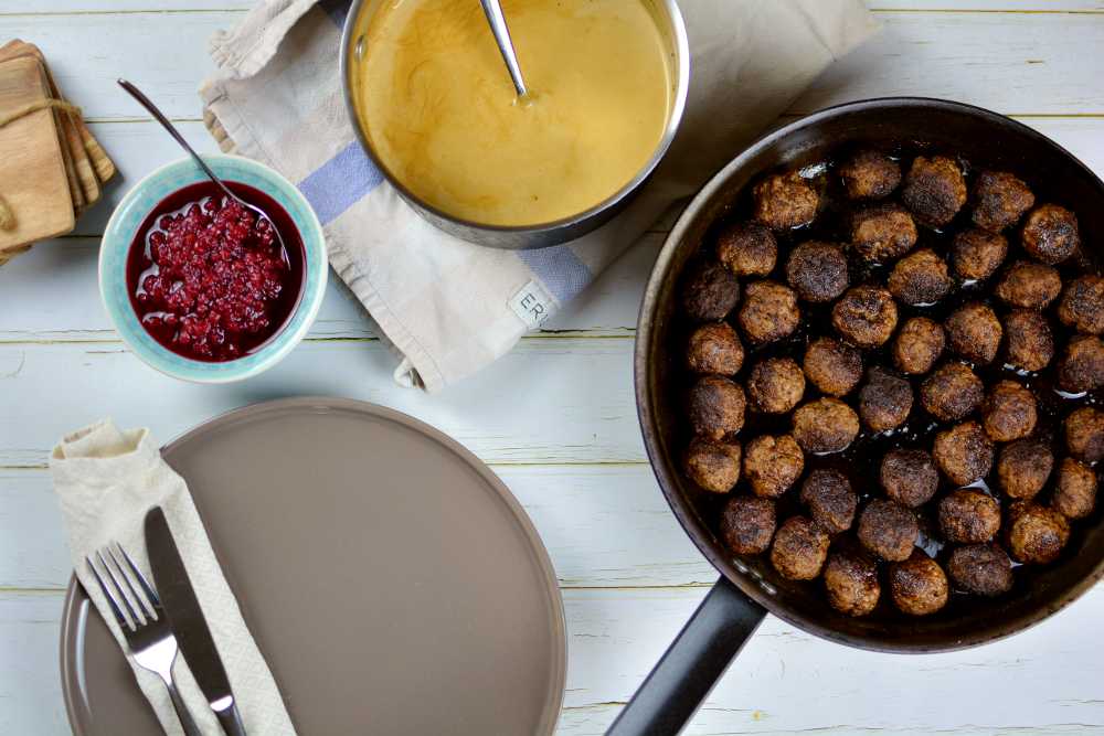 Köttbullar 9 Köttbullar i en stekpanna som ses uppifrån med en kastrull med sås och lite lingon bredvid.