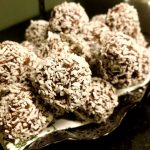 En skål med chokladbollar täckta av kokosflingor, placerade på en tallrik.
