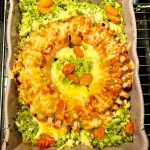 En ugnsform med ostgratinerad falukorv och broccolimos, dekorerad med aprikoser.