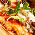 Närbild av pizza med tre ingredienser och färska grönsaker på toppen.