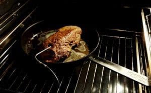 En köttbit som tillagas i en stekpanna i ugnen med en stektermometer.