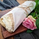 Semmelwrap inlindad i papper med grädde och en ros bredvid på en träskärbräda.