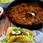 Tacoskal av ost fyllt med grönsaker och sås, placerat på en servett.