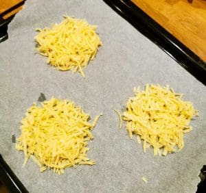 Tre högar av riven ost placerade på ett bakplåtspapper på en plåt.