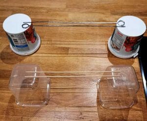 Två plastbehållare med en metalltråd som är spänd mellan dem, med två genomskinliga behållare under.