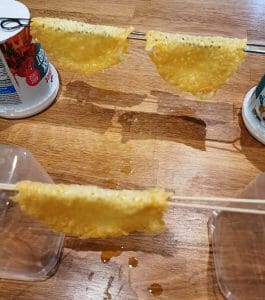 Tre tacoskal av ost hängande på pinnar över en yta med droppande vätska.