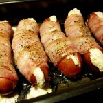 Fem baconlindade tjockkorvar med en vit fyllning, placerade i en ugnsform.