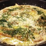 Fiskfiléer i en panna med dill och löksås, täckta av grädde och örter.