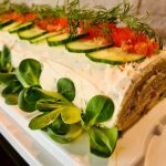 Laxrulle med skivor av gurka, tomat och dill på toppen, serverad på en vit platta.