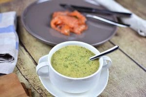 Skål med gravlaxsås innehållande dill och senap, med en sked i. Bakom syns en tallrik med gravad lax.