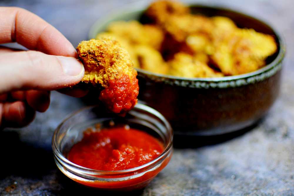 Krispiga blomkålstoppar 3 En hand som håller i en krispig blomkålstopp och doppar den i lite chilisås.