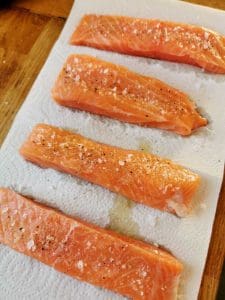 Fyra laxfiléer som ligger på en pappershandduk, kryddade med salt och peppar.