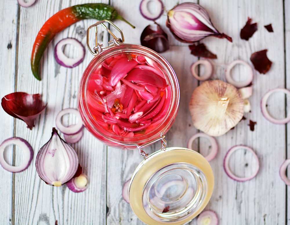 Picklad rödlök (utan socker) 12 En burk med picklad rödlök sedd uppifrån med lök, chili och vitlök utspritt runt burken.
