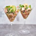 Två martiniglas fyllda med skaldjur, lime och grönsaker, placerade på en yta.