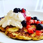 Amerikanska pannkakor toppade med vispad grädde, blåbär och jordgubbar på en tallrik.