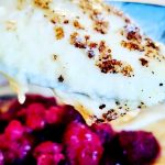 En sked med gräddgrot som har en gyllene yta, med hallon i bakgrunden.