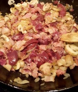 En blandning av kycklinglever, svamp, lök och bacon i en stekpanna.