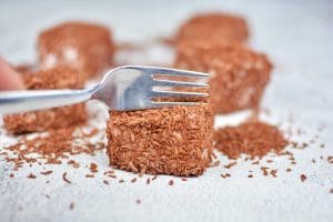 En gaffel som skär i en chokladpralin täckt med kokosflingor.