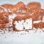 Kokosgodis täckt med chokladflingor på en yta med några bitar i bakgrunden.