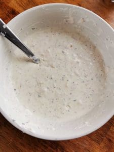 En skål med en gräddig såsblandning som innehåller kryddor och örter.