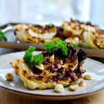 Grillad vitkålsslice med nötter och grönsaker på en tallrik.