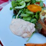 En portion hamburgerdressing placerad på en tallrik med grönsallad och tomat.