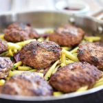Köttfärsbiffar som steks tillsammans med grönsaker i en stor stekpanna.
