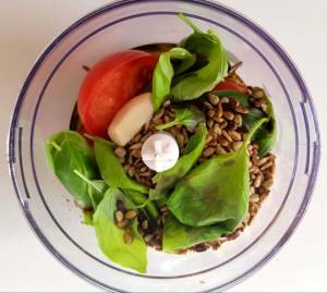 Ingredienser för röd pesto i en matberedare, inklusive tomat, basilika och solrosfrön.