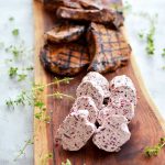 Grillade köttbitar och smör med örter på en träskärbräda.