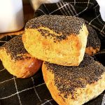 Tre bitar bröd med vallmofrön på toppen, placerade på en svart och vit rutad duk.